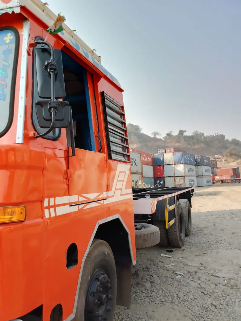 Side of an orange truck cab with container stacks in the yard behind