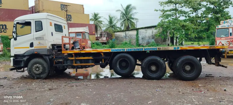 White truck with a long multi-axle flatbed trailer parked beside palm trees