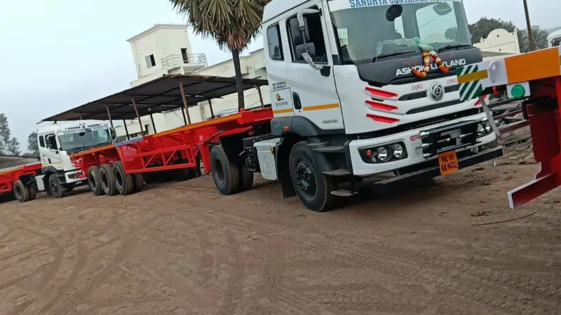 New white tractor unit with a red trailer parked at a transport depot