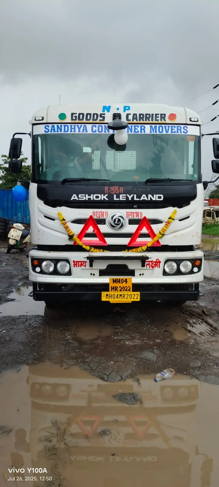 New Sandhya Container Movers tractor unit decorated with a garland, reflected in a rain puddle