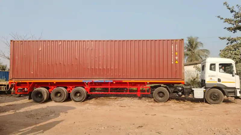 A 40ft container seated on a red three-axle trailer coupled to a white Sandhya tractor