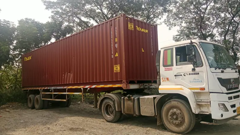 Tractor unit with a 40ft maroon container on a trailer, parked under trees