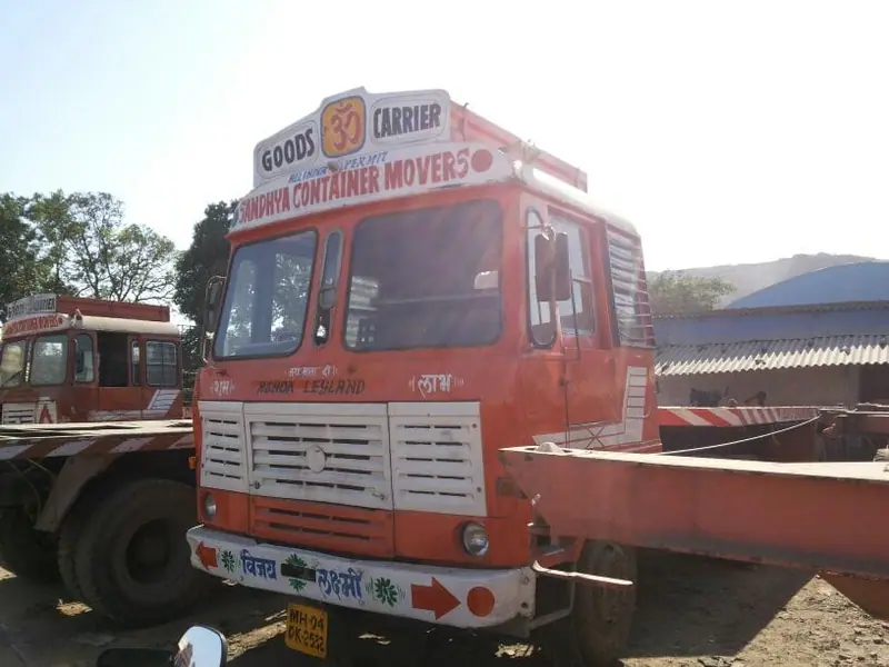 Orange Sandhya Container Movers truck with a flatbed body in a yard