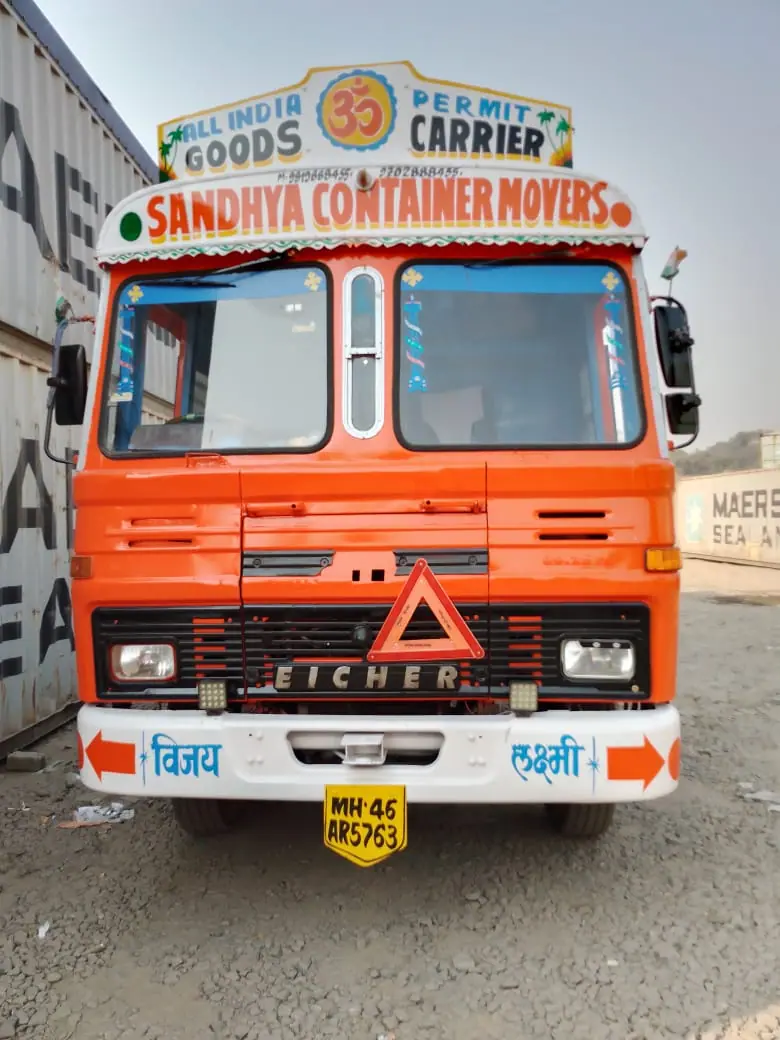 Orange Sandhya Container Movers truck parked beside stacked shipping containers