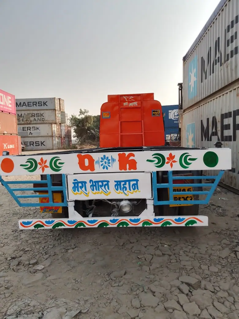 Rear of a decorated truck in a container yard with stacked containers on either side