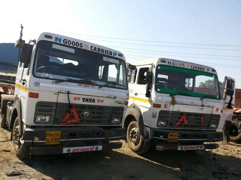 Two white goods-carrier trucks parked side by side in a yard